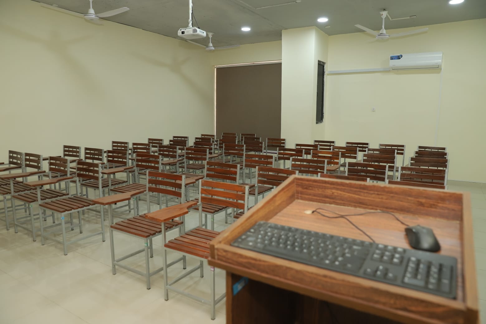 campus facilities in KIHS-Well-lit, ventilated classroom featuring arranged chairs and a rostrum with keyboard setup for interactive teaching.