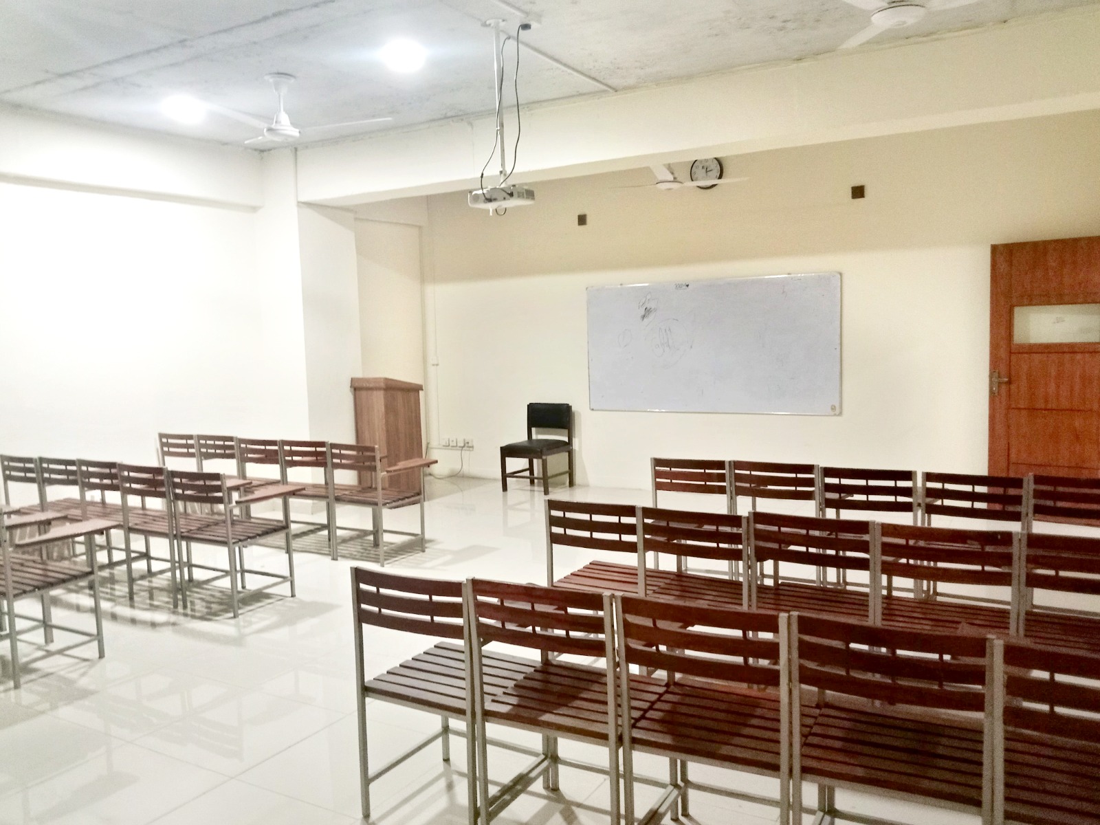 campus facilities in KIHS - Modern classroom featuring bright lighting, ample ventilation, organized seating, and teaching tools like a rostrum and whiteboard.
